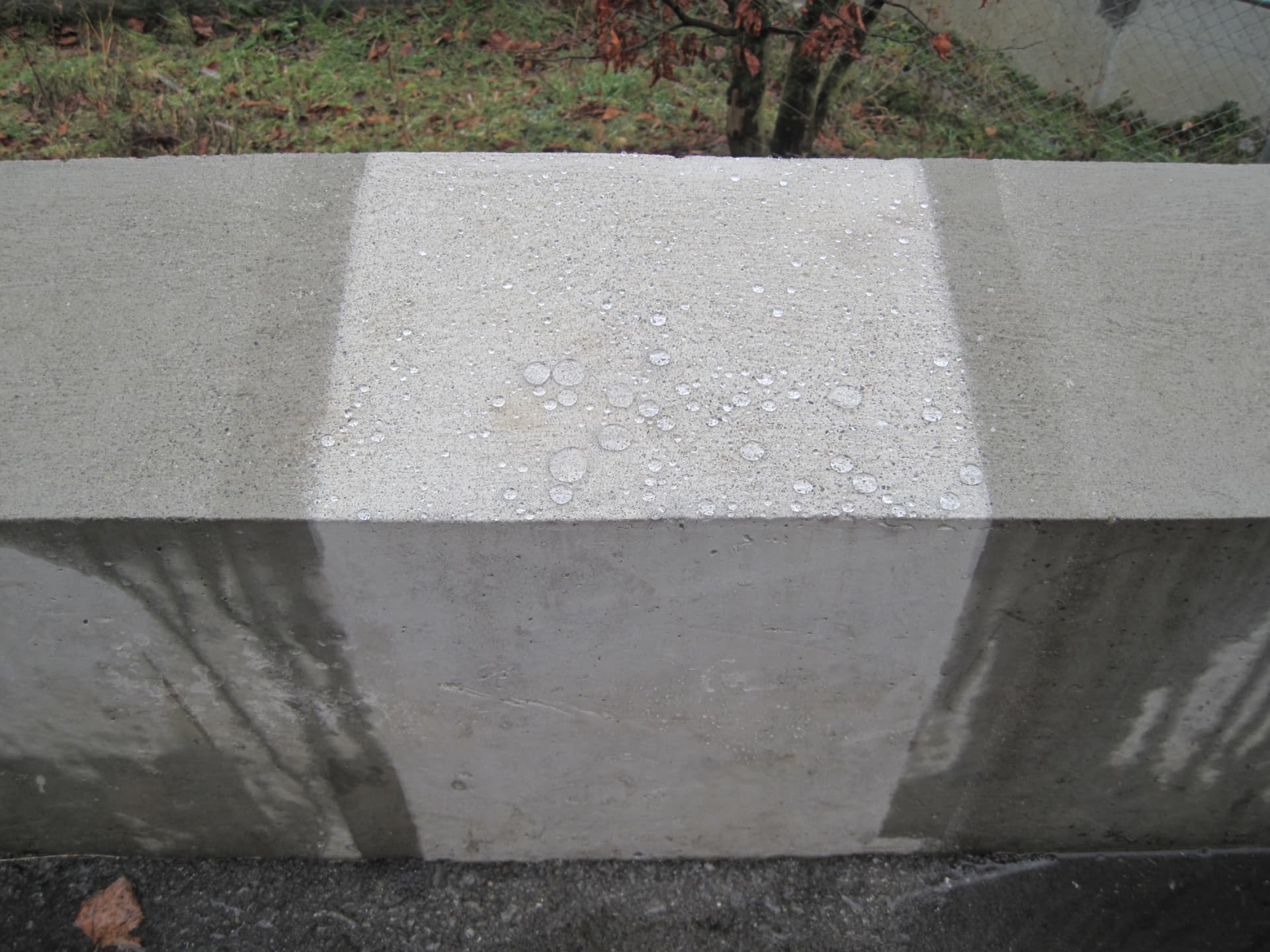 Partly treated concrete wall: water beads up on the impregnated area, while the untreated part absorbs it and darkens.